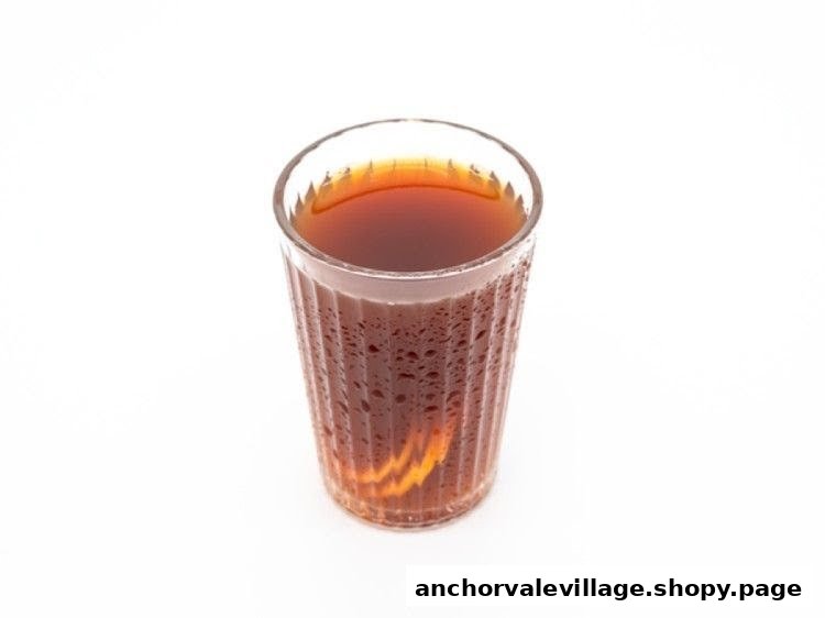 A clear glass of dark beverage, possibly tea or coffee, with condensation, on a white background.