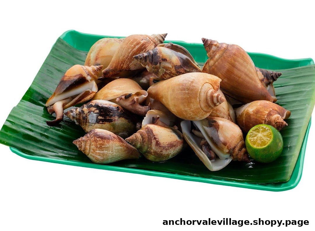 A plate of cooked sea snails or conch with a lime wedge on a banana leaf.