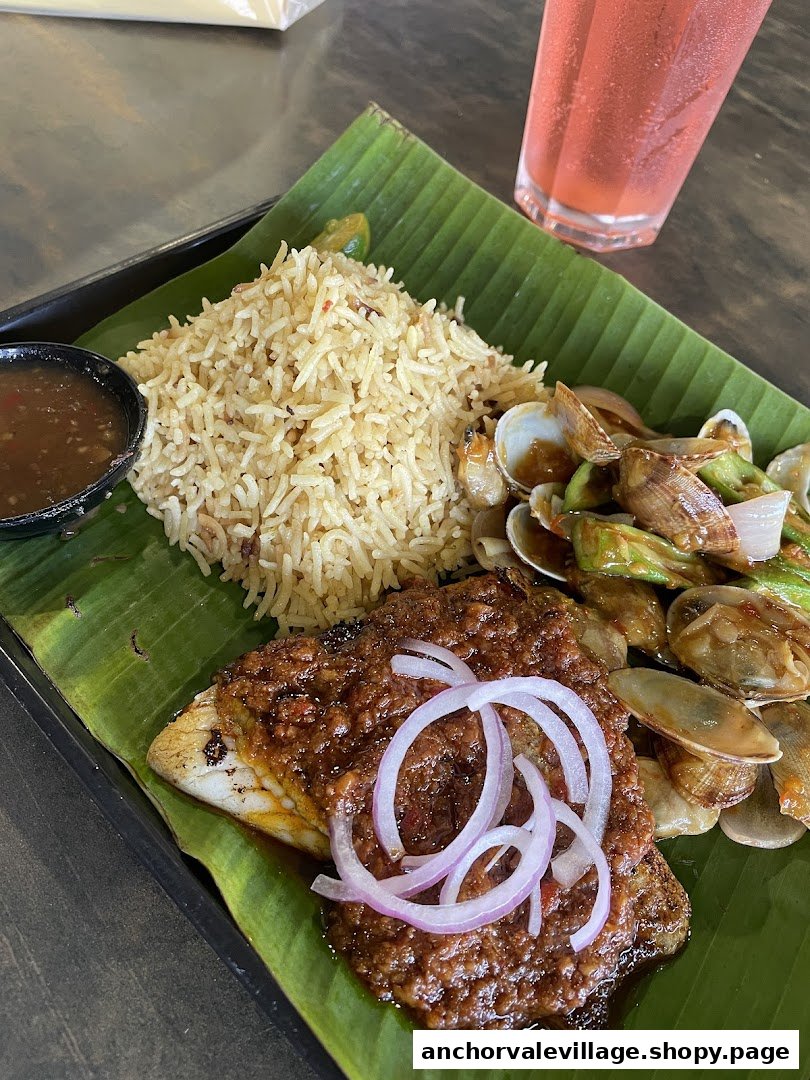 A delicious meal featuring grilled fish, fragrant rice, clams, and a refreshing drink, served on a banana leaf.