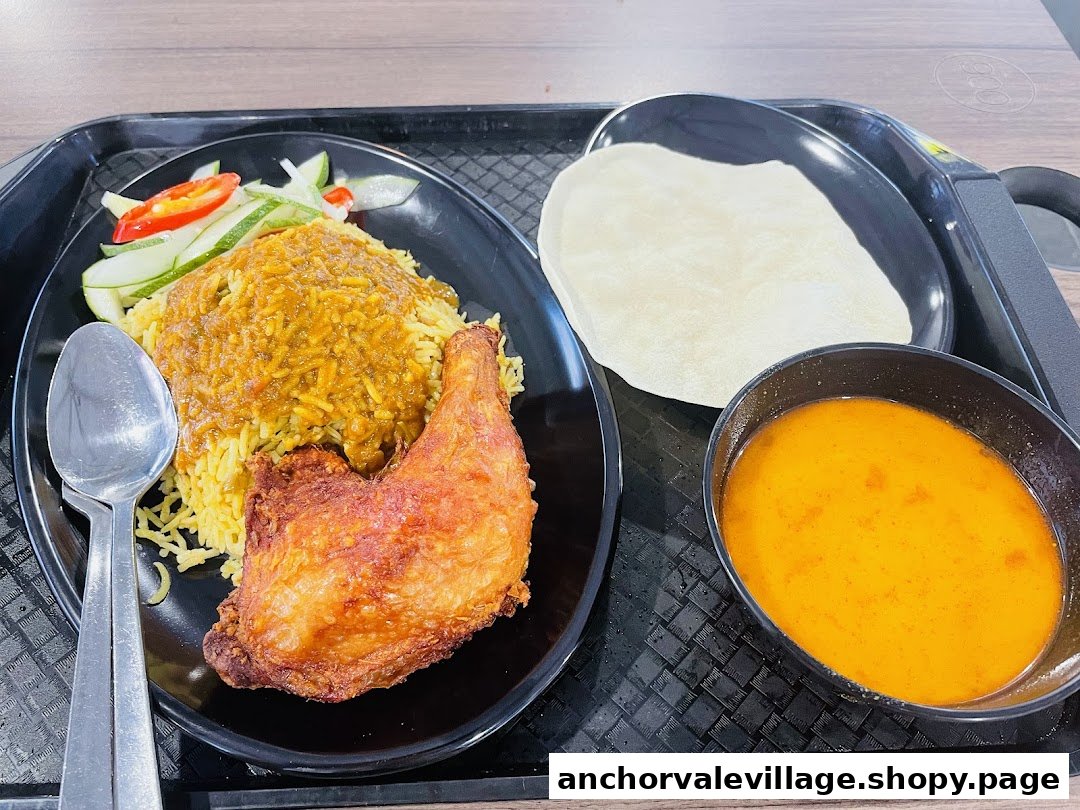 A delicious plate of biryani with fried chicken, curry, and flatbread on a black tray.