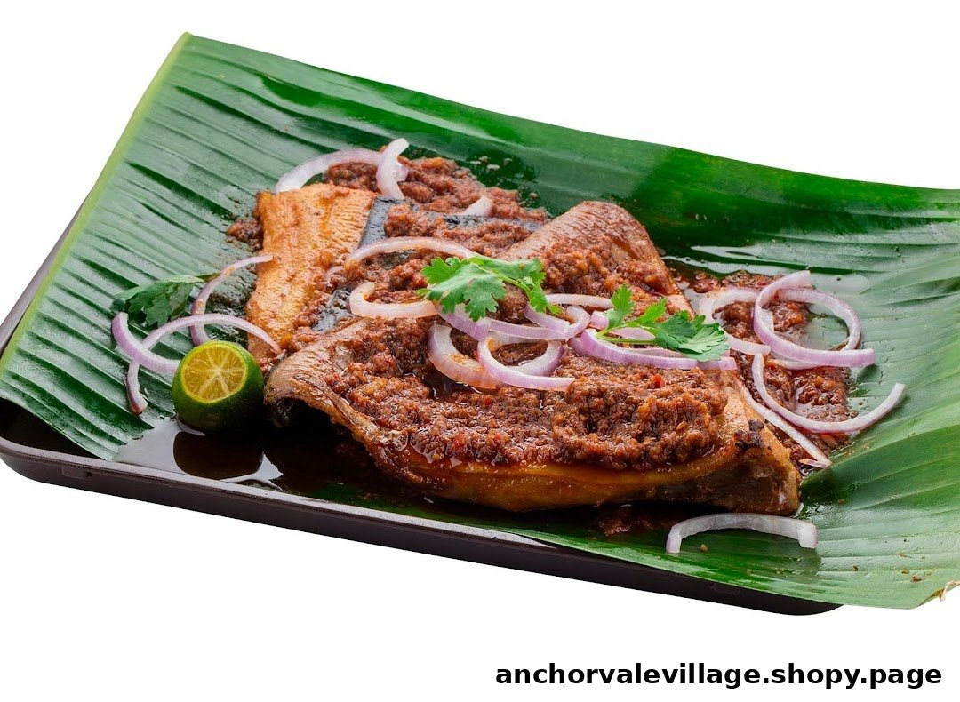 A grilled fish dish served on a banana leaf, topped with sauce, red onions, and a lime wedge.