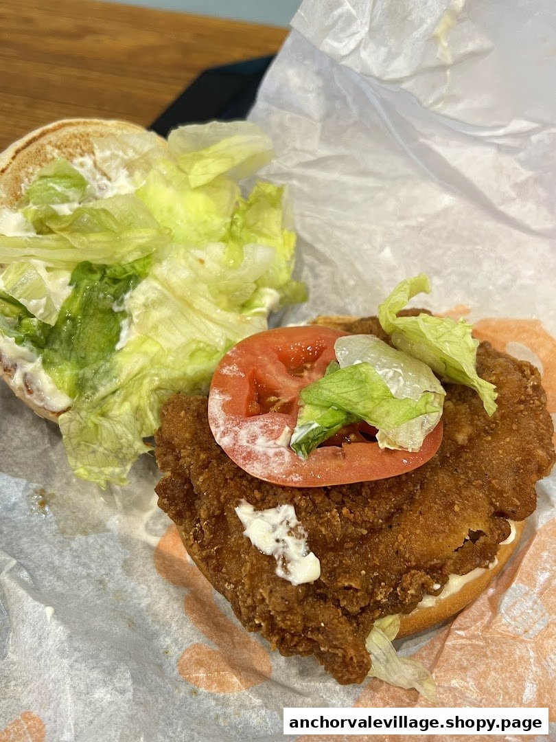 A close-up of an open crispy chicken sandwich with lettuce, tomato, and mayonnaise.