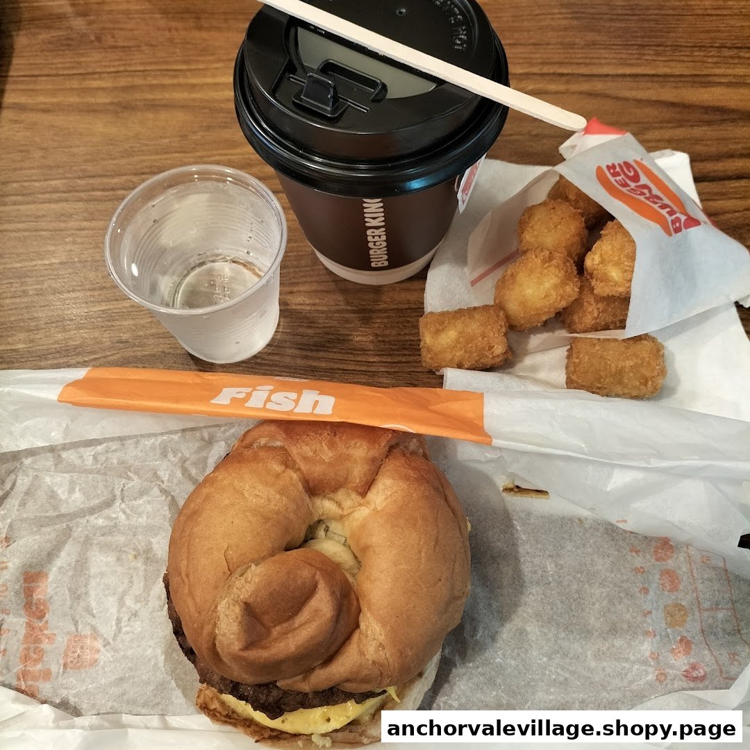 A Burger King meal featuring a burger, tater tots, a drink, and a cup of water on a wooden table.