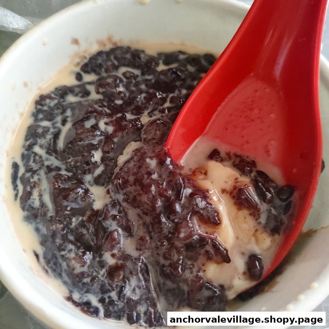 A close-up of a bowl of black glutinous rice dessert with a red spoon, revealing creamy tofu pudding.