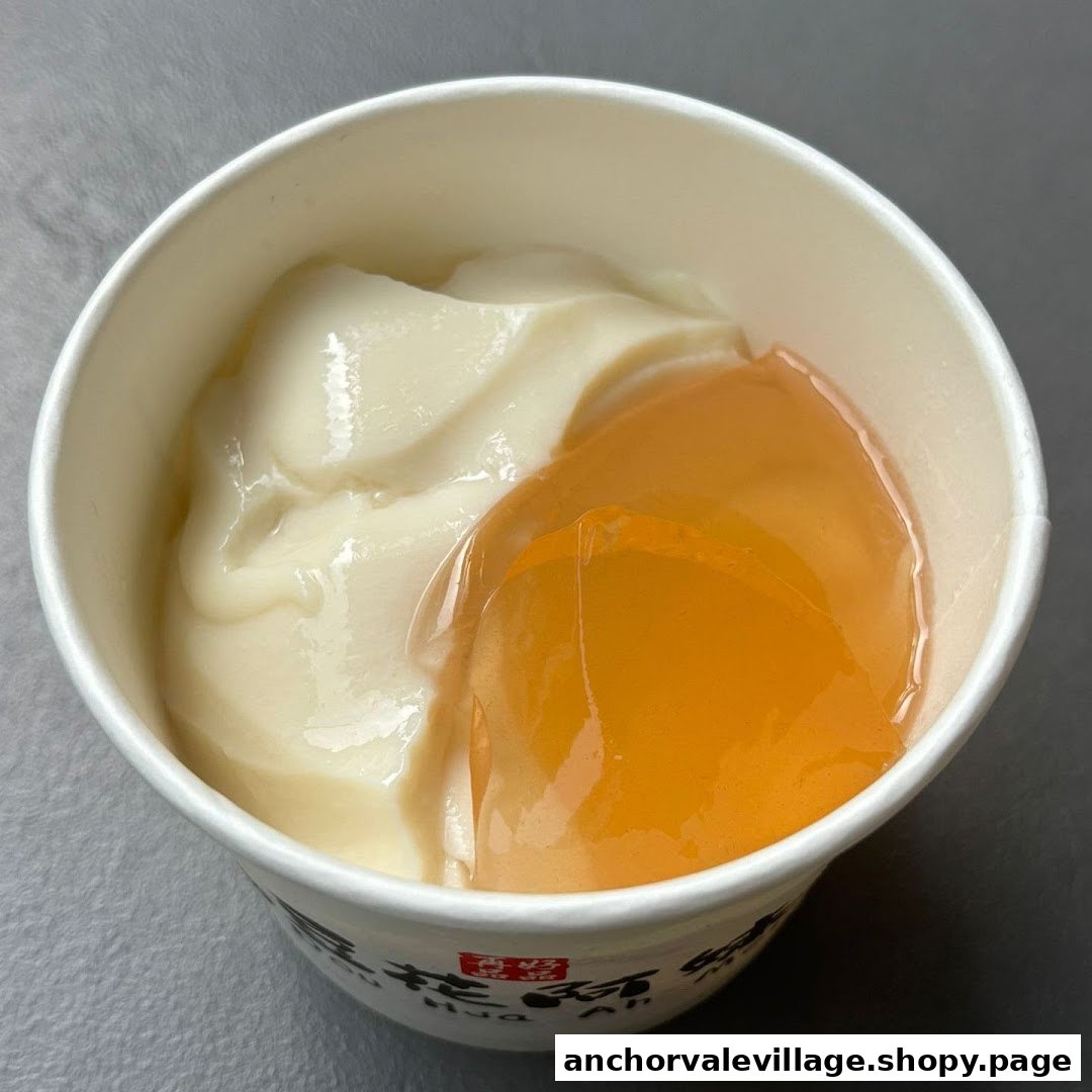 A close-up of a cup of smooth dou hua (tofu pudding) with a clear, amber-colored topping.