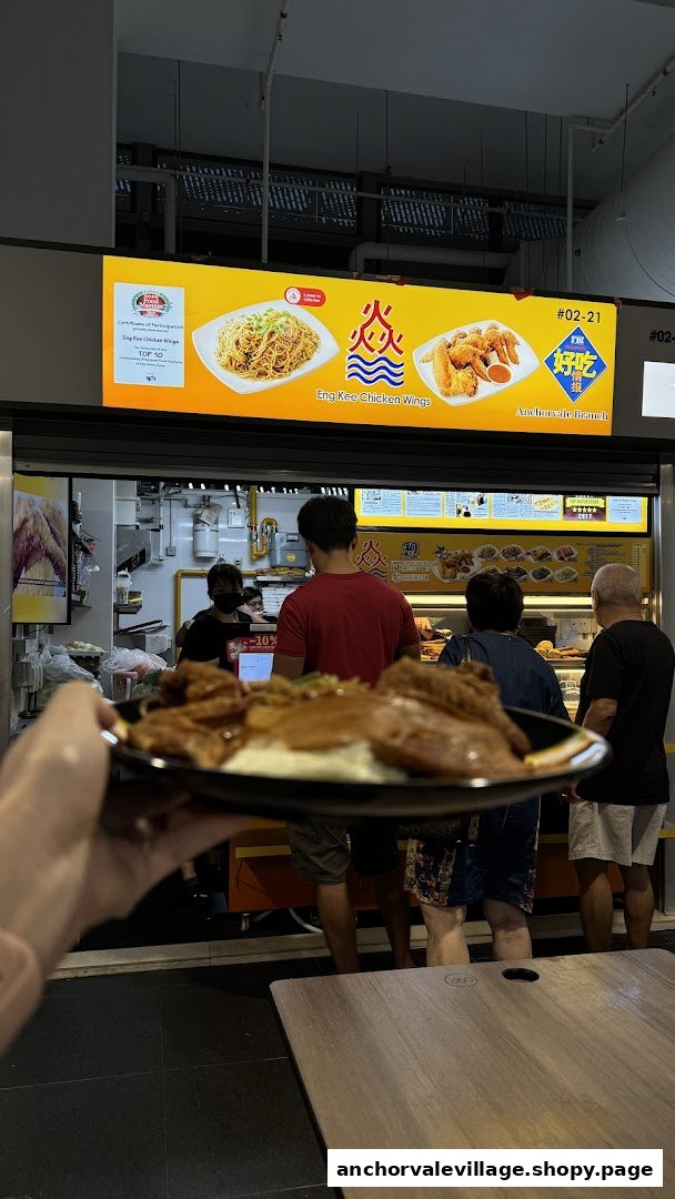 A customer holds a plate of food in front of Eng Kee Chicken Wings stall with people queuing.
