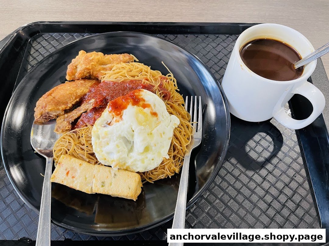 A plate of fried noodles with crispy chicken wings, fried egg, fish cake, and a cup of coffee.