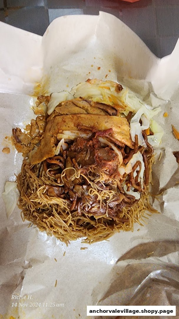 A close-up of fried noodles with various toppings, served in a paper wrapper.