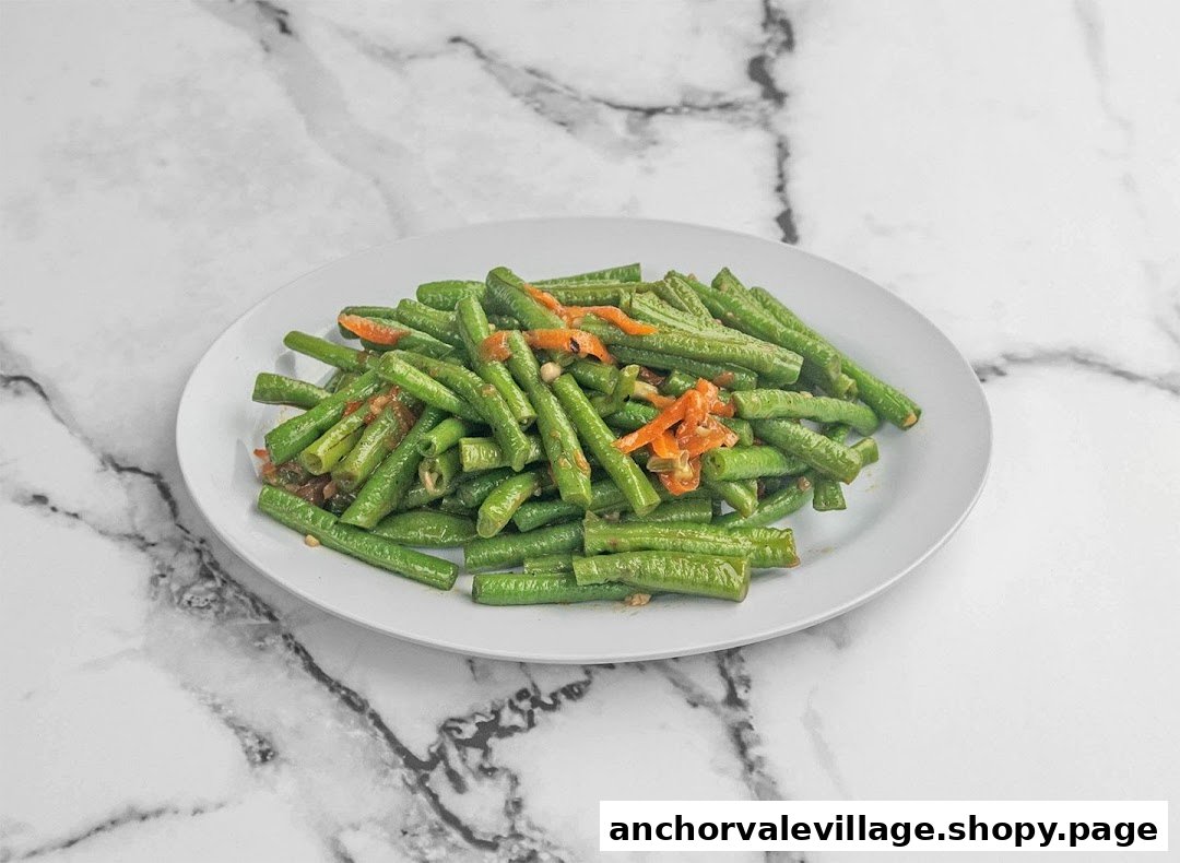 A plate of stir-fried long beans with chili and garlic on a white marble background.