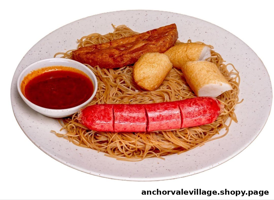 A plate of stir-fried vermicelli with fried fishcakes, sausage, and a side of chili sauce.