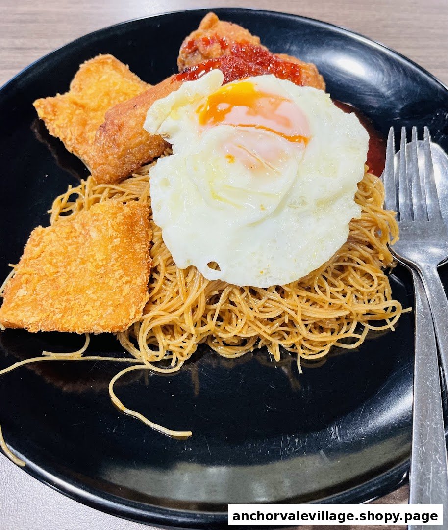 A plate of noodles with fried chicken wings, fish cake, and a sunny-side-up egg.