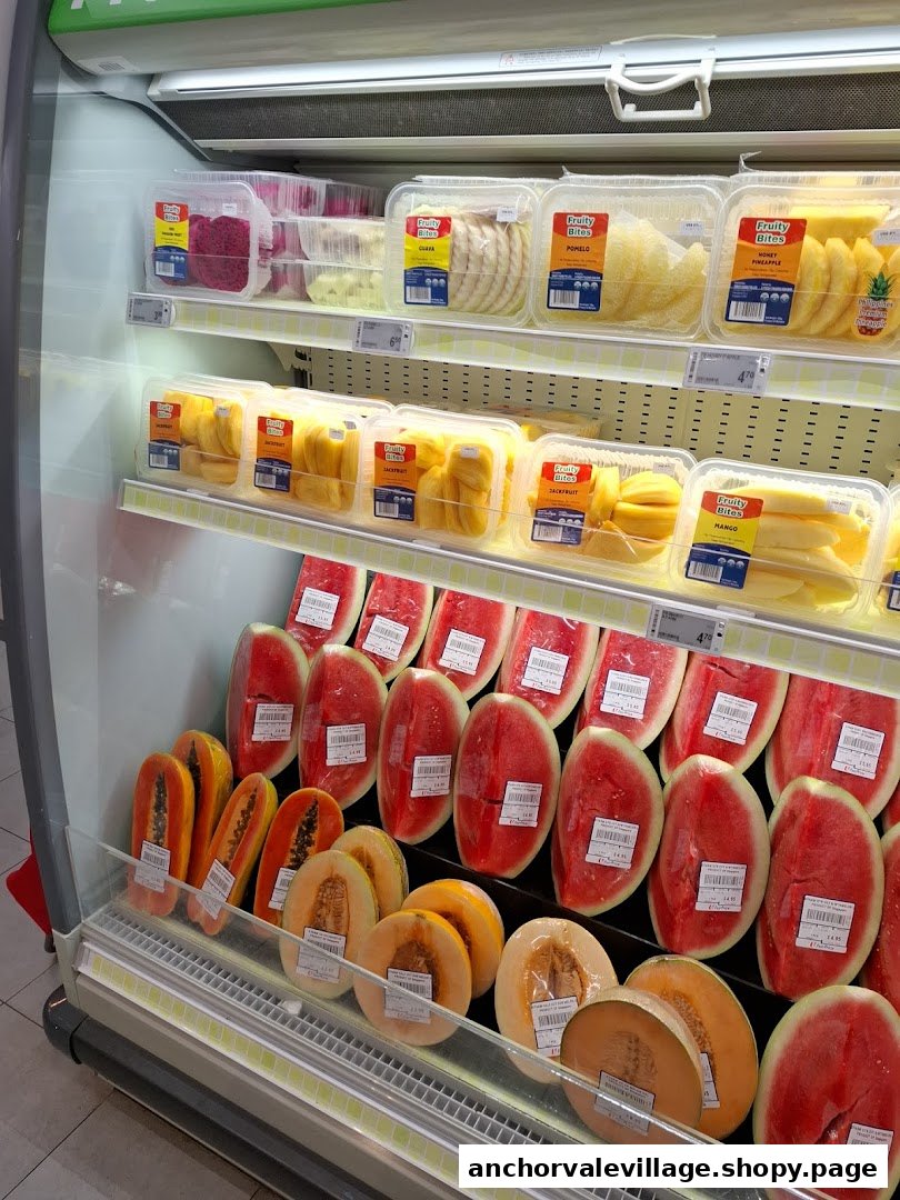 A supermarket refrigerated display featuring various fresh cut fruits and whole melons and watermelons.