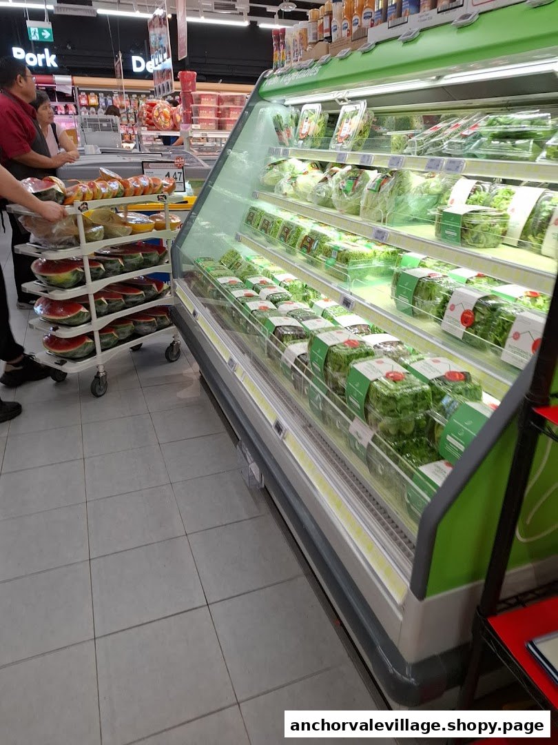 A supermarket aisle featuring a vibrant fresh produce display and a customer with a cart of watermelons.