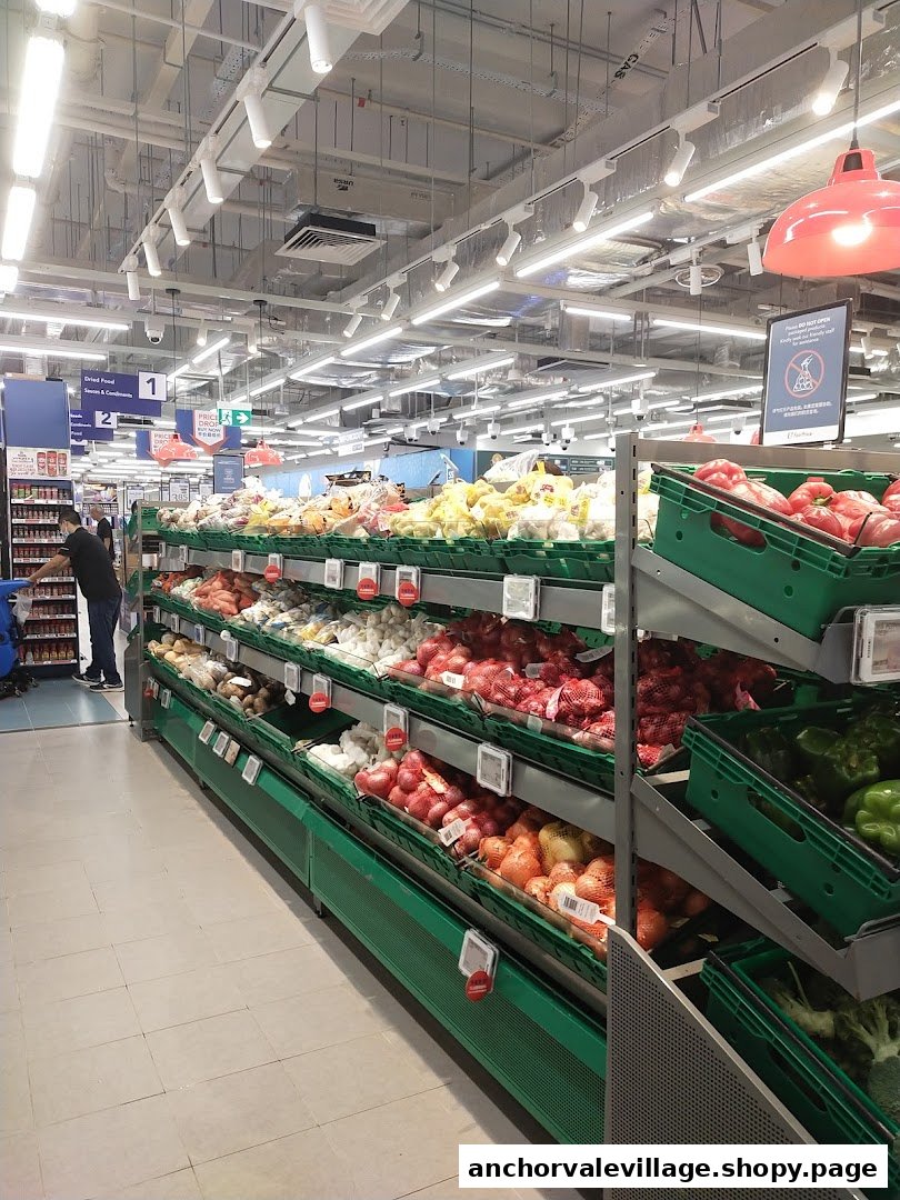 An aisle inside a supermarket featuring a wide selection of fresh produce like onions, potatoes, and bell peppers.