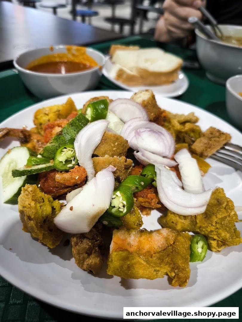 A close-up of a vibrant plate of rojak, featuring fried fritters, onions, and green chilies.