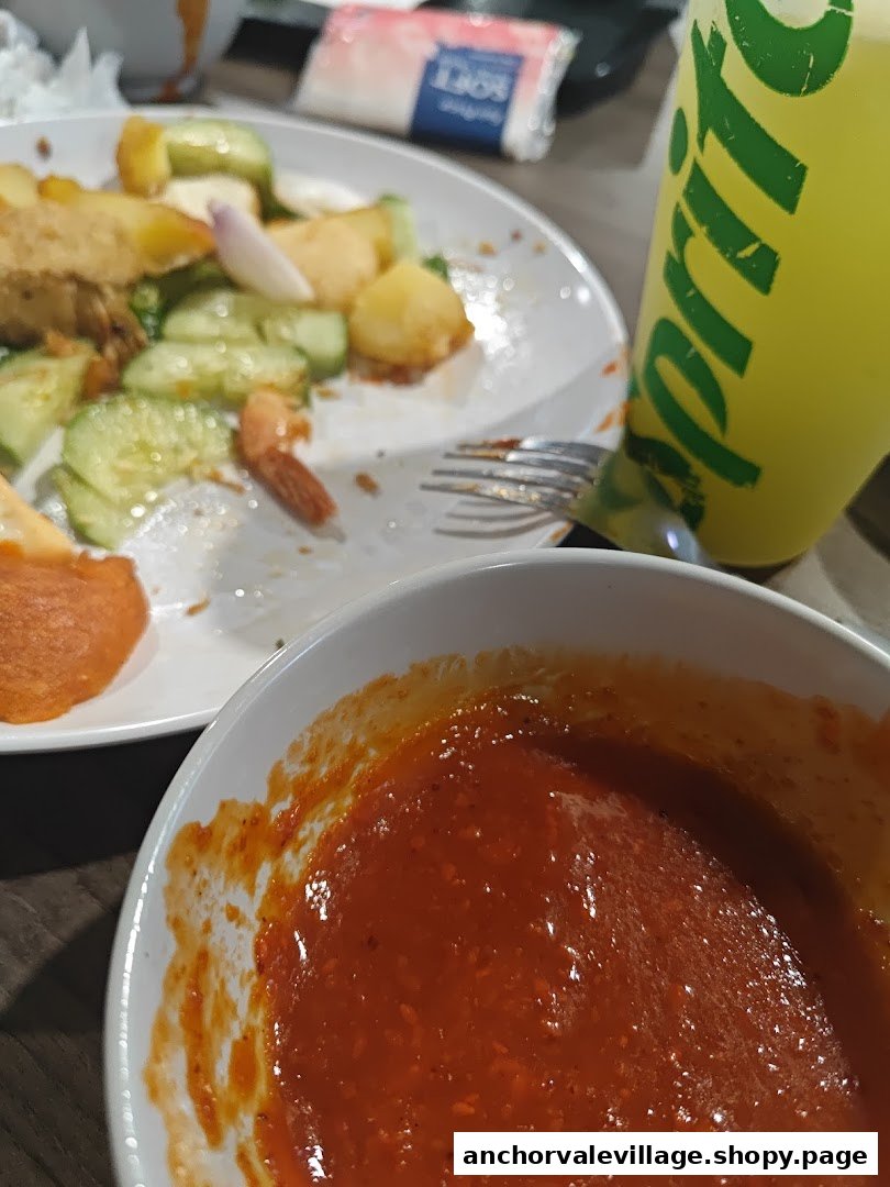 A close-up of a partially eaten plate of rojak with a bowl of sauce and a drink.