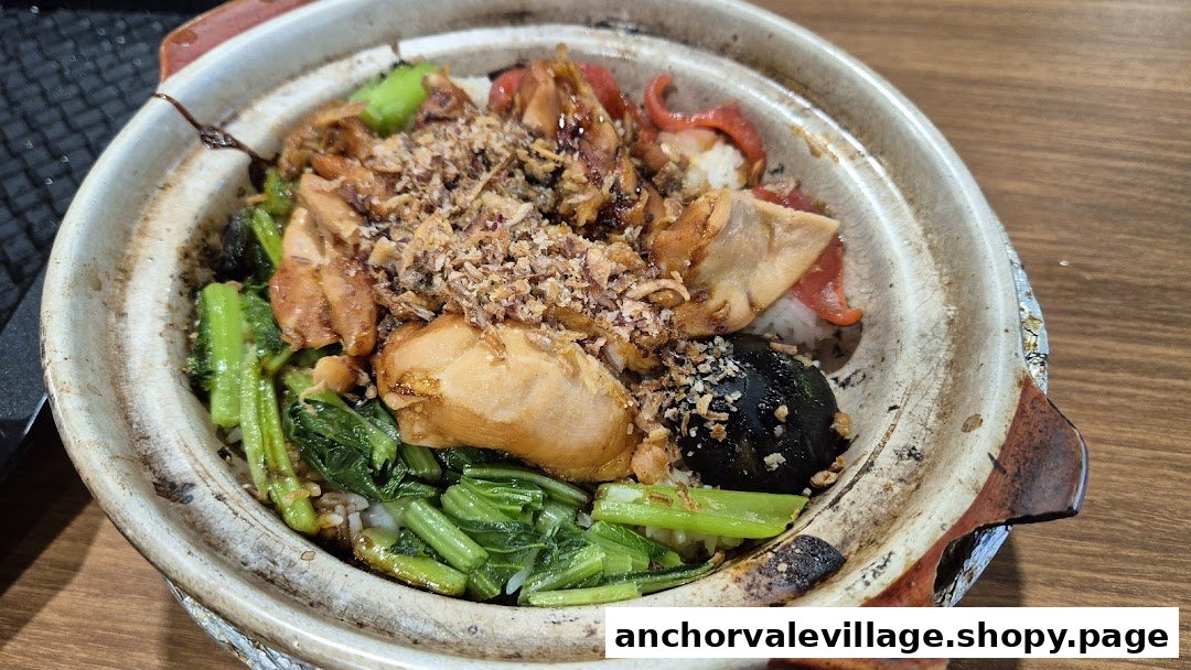 A close-up of a sizzling claypot rice dish with chicken, vegetables, and crispy toppings.