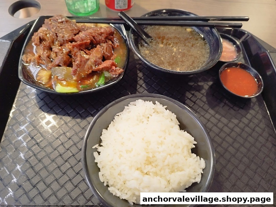 A hearty meal featuring braised beef, fluffy rice, soup, and dipping sauces on a serving tray.