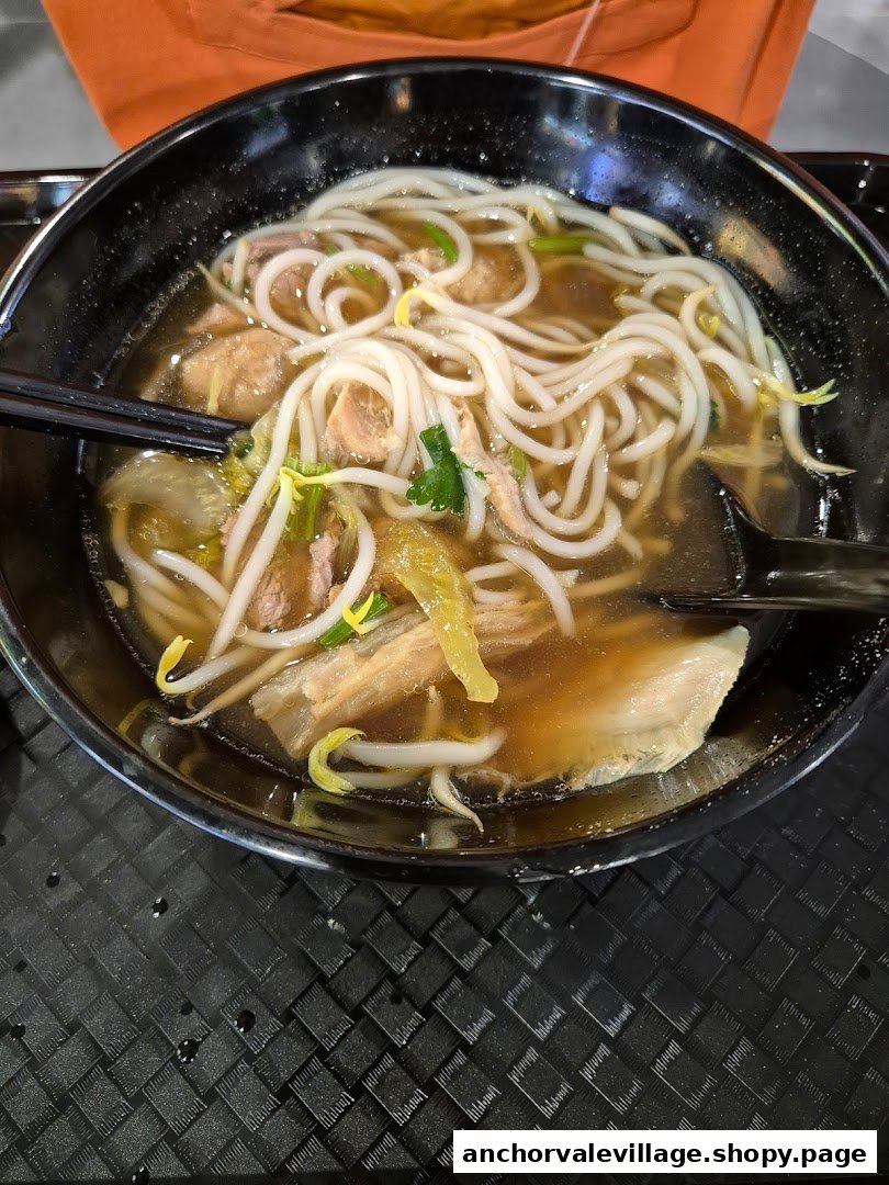 A close-up of a delicious bowl of Hainan beef noodles with broth, meat, and vegetables.