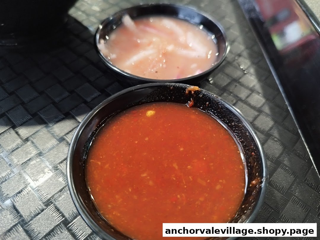 Two small bowls of dipping sauces, one red chili-based and one lighter, on a textured table.