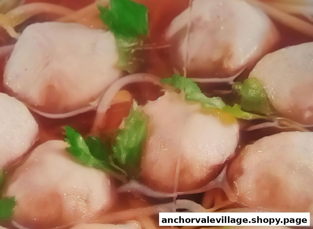 Close-up of tender fish balls or dumplings in a rich, reddish broth with fresh greens.