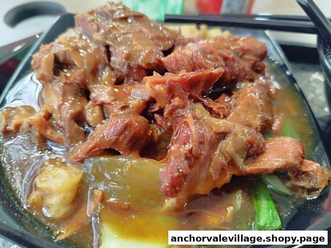 A close-up of a hearty beef dish with rich sauce and vegetables in a black bowl.