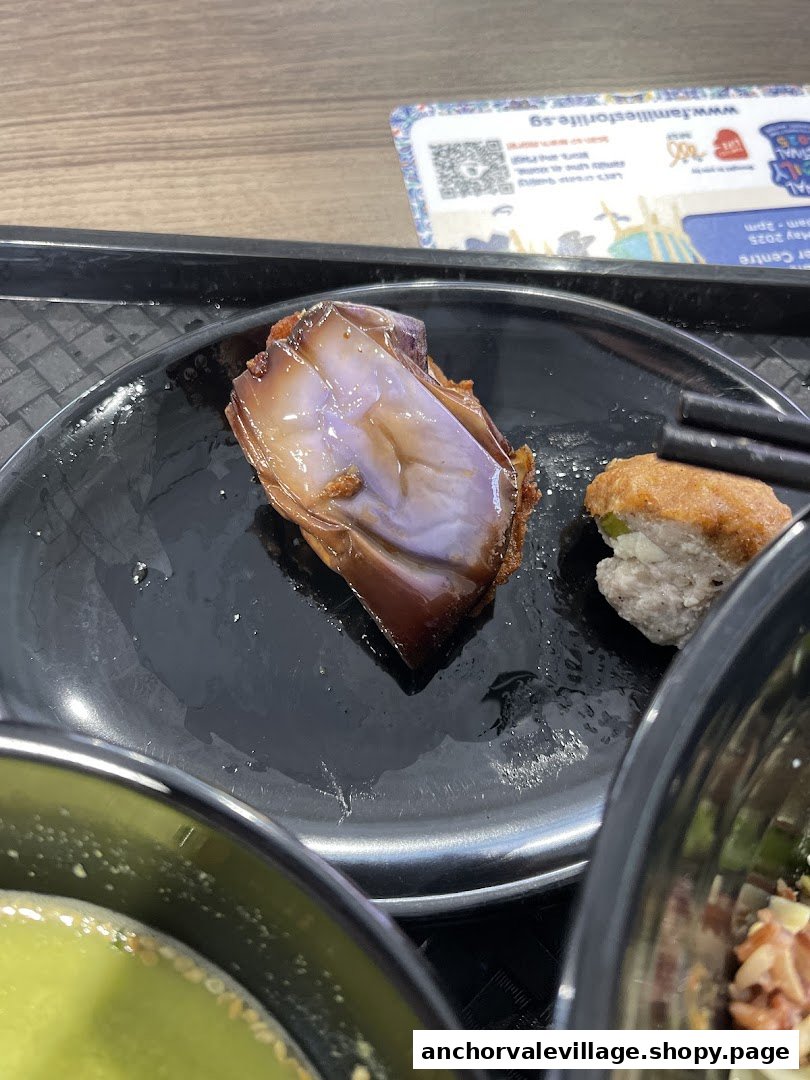 A close-up of a braised eggplant and another fried item on a black plate, served at Hakka Leipopo.