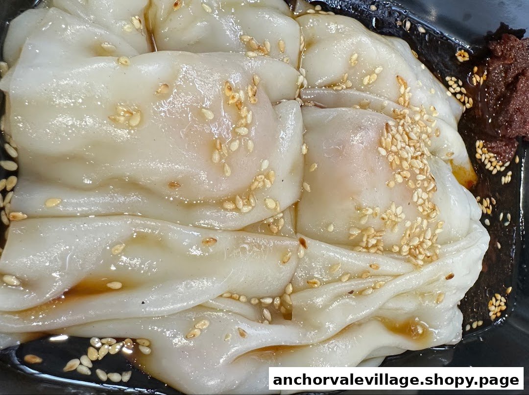 Close-up of Hong Kong style Chee Cheong Fun with sesame seeds, savory sauce, and chili paste.