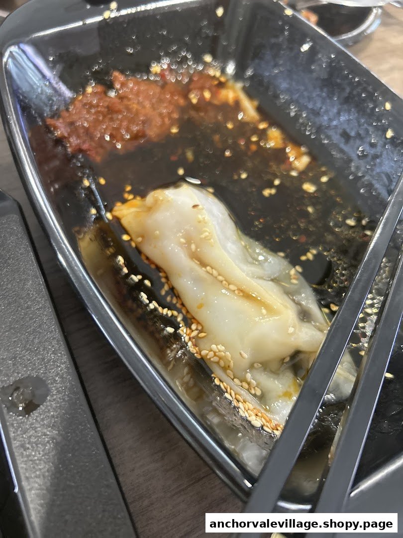 A close-up of a partially eaten Hong Kong style Chee Cheong Fun with chili sauce and sesame seeds.