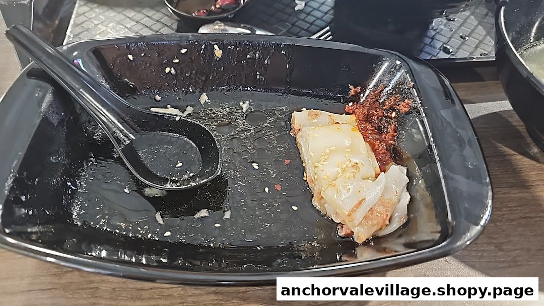 A black plate with a partially eaten Hong Kong style chee cheong fun and a spoon.