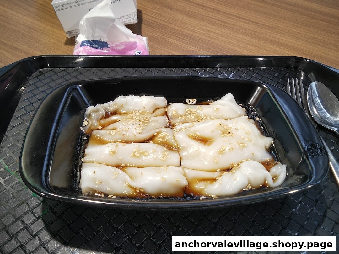 A close-up of Hong Kong style Chee Cheong Fun with savory sauce and sesame seeds on a black tray.