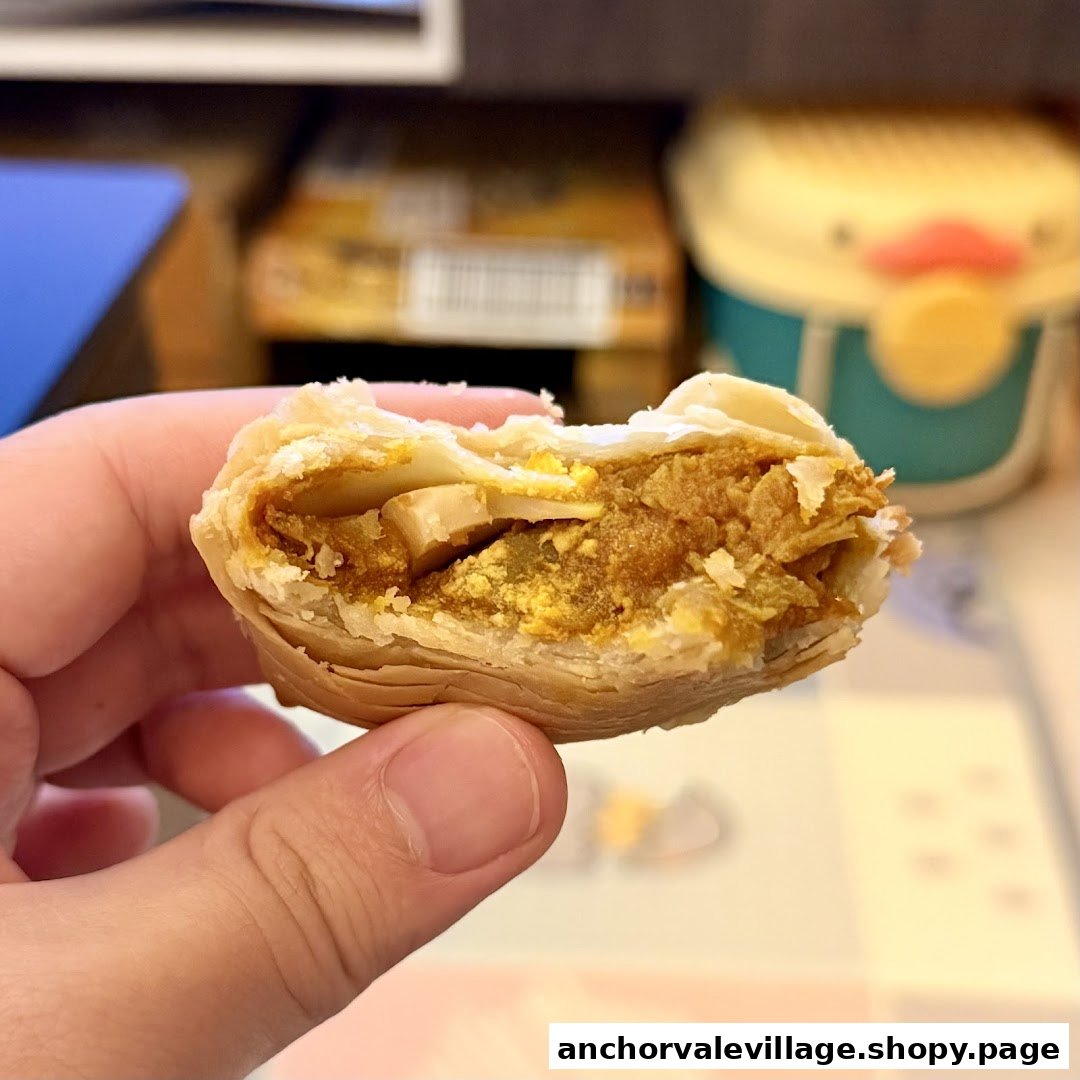 A hand holds a freshly bitten curry puff, revealing its rich, savory filling and flaky pastry.
