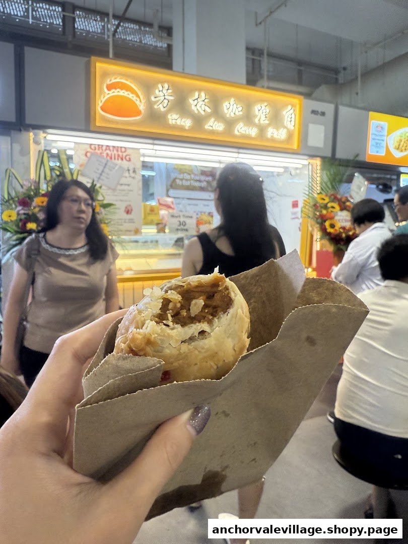 A hand holds a freshly baked curry puff in front of the Hong Lim Curry Puff stall.