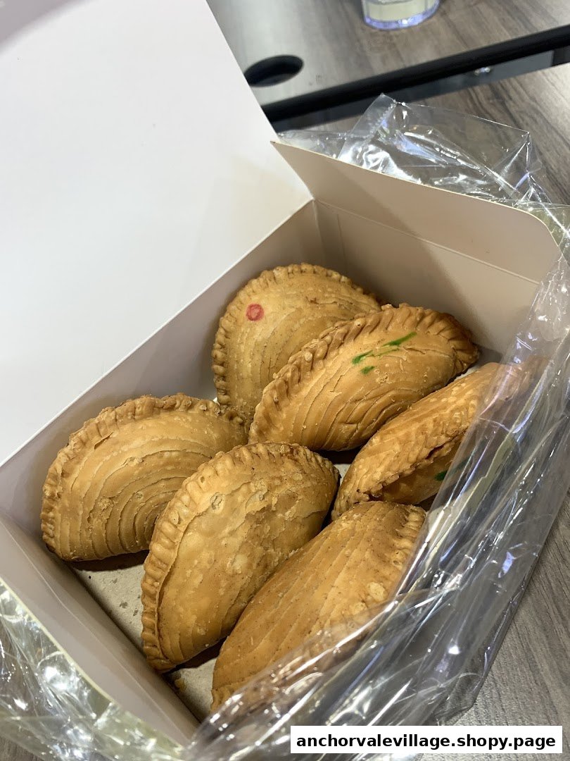 A box of freshly baked curry puffs with flaky crusts, some marked with red or green dots.