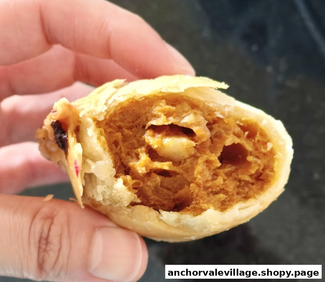 A hand holds a freshly bitten curry puff, revealing its rich, savory curry filling.