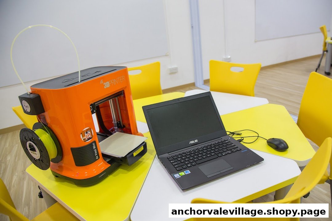 A 3D printer and laptop on a yellow and white table in a modern learning center.