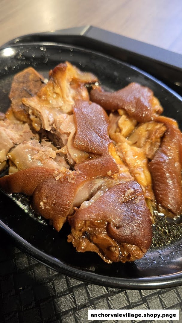 A close-up of succulent braised pig trotters served on a black plate.