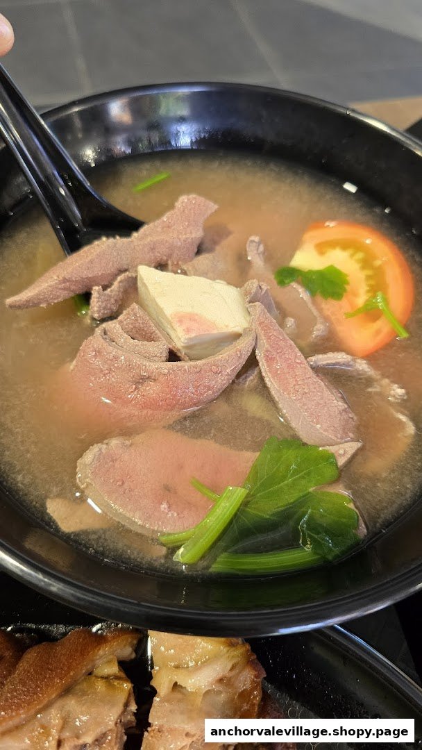 A close-up of a bowl of pig organ soup with various organs, tofu, and vegetables, next to braised pig trotters.