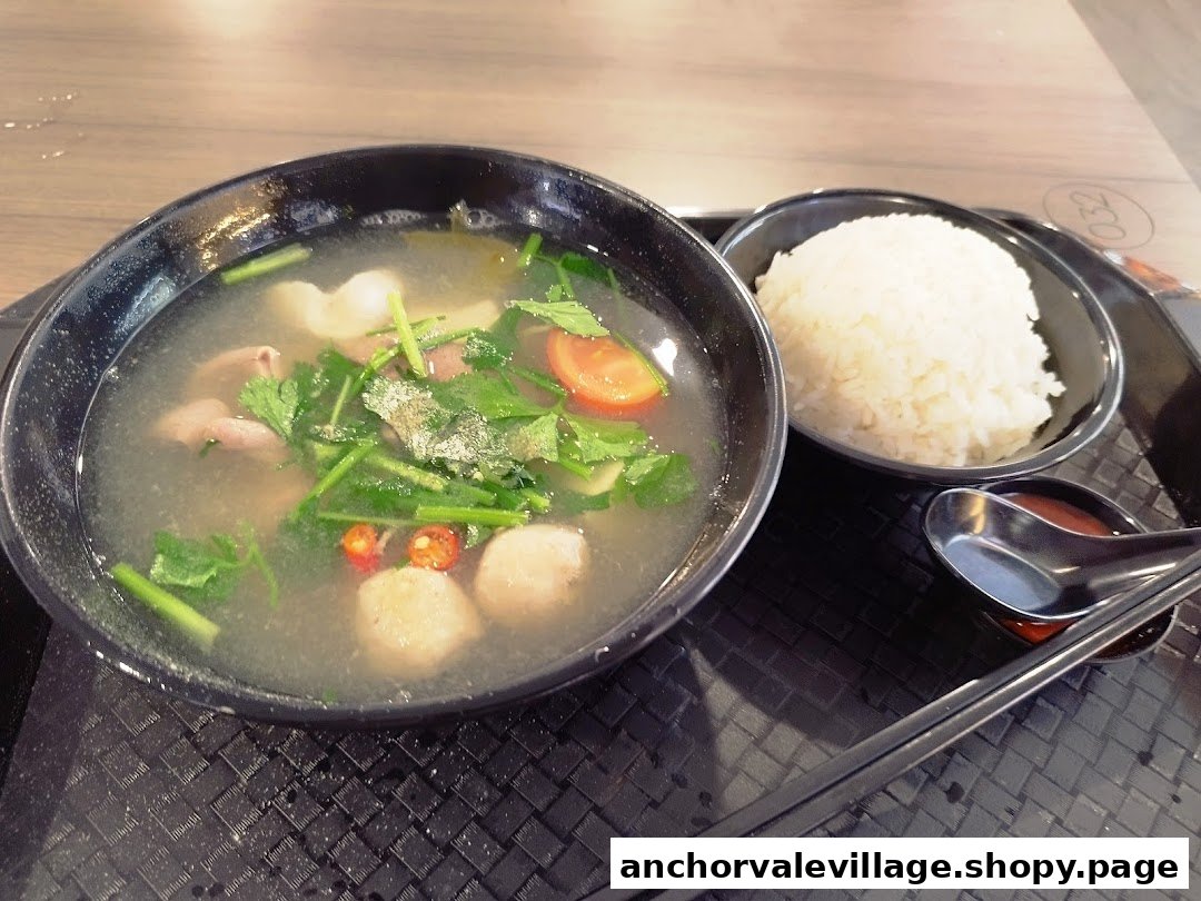 A hearty bowl of clear soup with pig organs, meatballs, vegetables, and a side of rice.