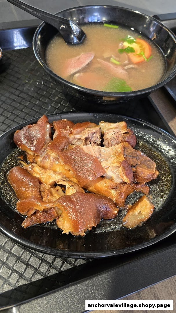 A close-up of a plate of braised pig trotters and a bowl of soup with meat and vegetables.