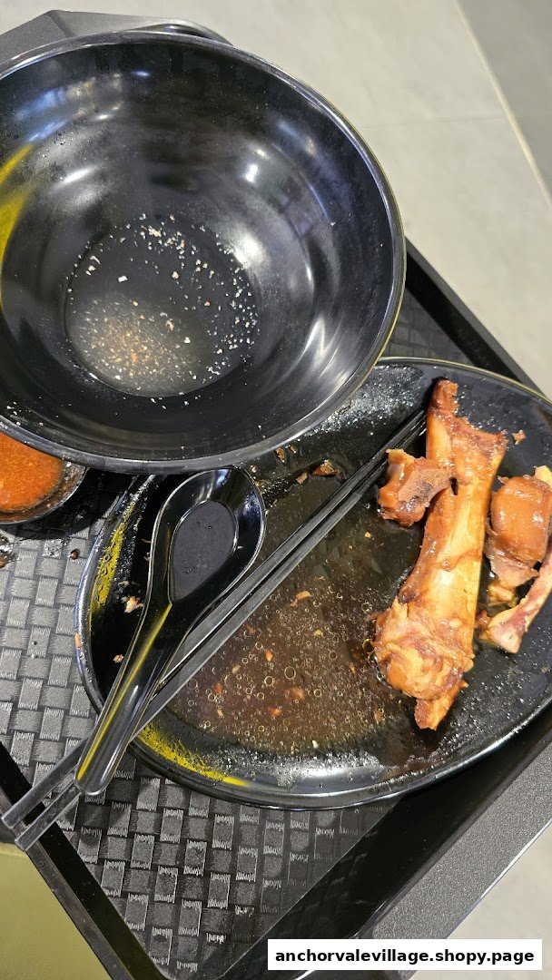 A used bowl and plate with food remnants, chopsticks, and a spoon on a tray after a meal.