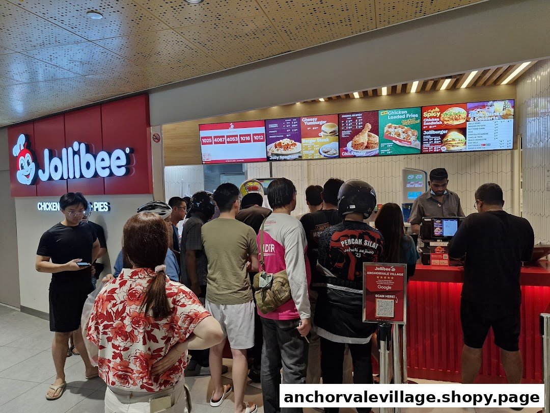 Customers queueing at the counter of a busy Jollibee restaurant with digital menu boards visible.