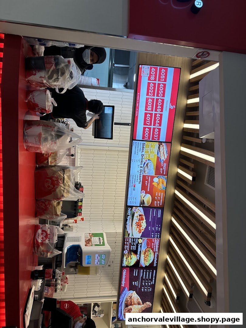 Busy Jollibee counter with staff, digital menu boards, and order pickup area.