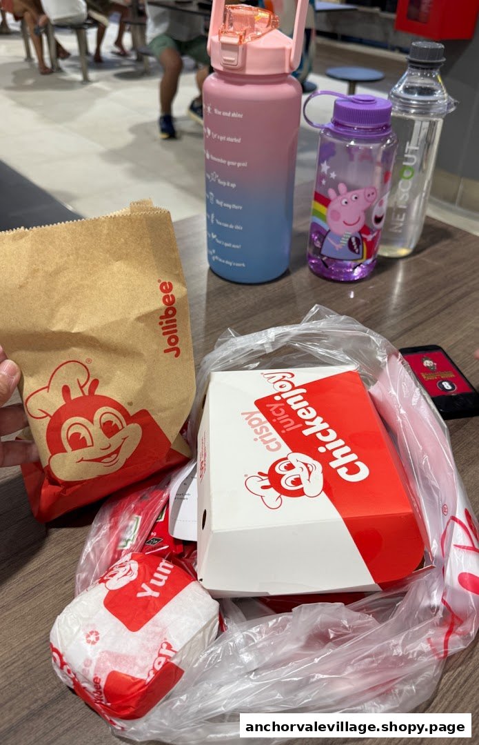 Jollibee food items in branded packaging on a table with water bottles, ready to be enjoyed.