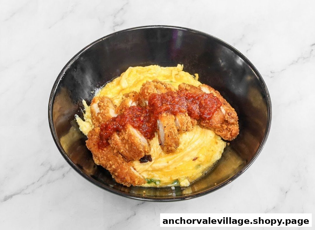 A close-up of a delicious bowl featuring crispy fried chicken cutlets, fluffy scrambled eggs, and a vibrant red sauce.