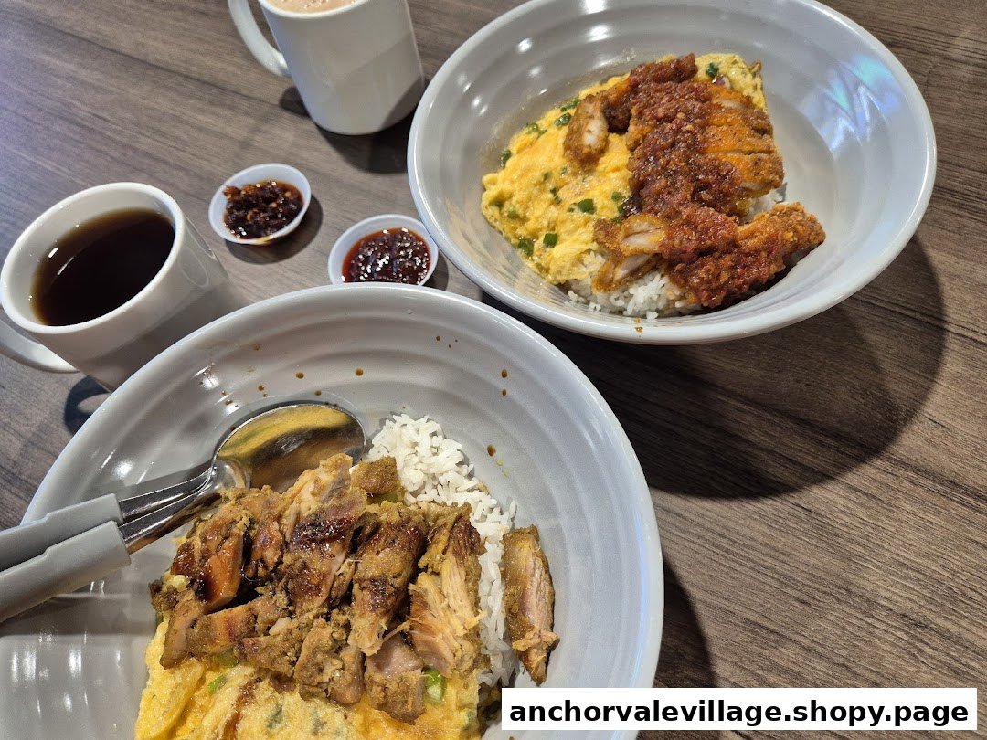 Two delicious rice bowls with meat, egg, and accompanying drinks and chili on a wooden table.