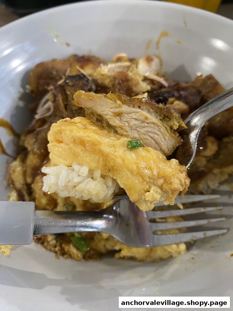 A close-up of a fork lifting a delicious piece of chicken, omelette, and rice from a bowl.