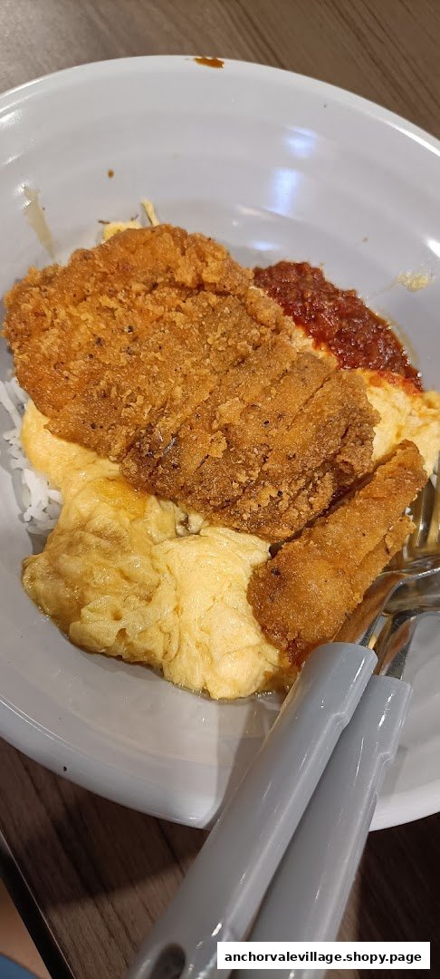 A close-up of a delicious fried cutlet dish with fluffy scrambled eggs, rice, and chili sauce.