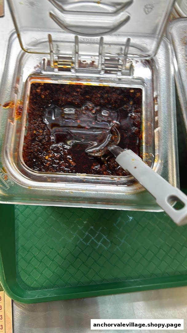 A close-up of a clear container filled with spicy chili oil and a serving spoon.