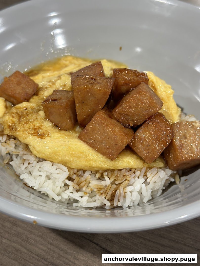 A close-up of a delicious rice bowl topped with fluffy omelette and savory cubed meat.